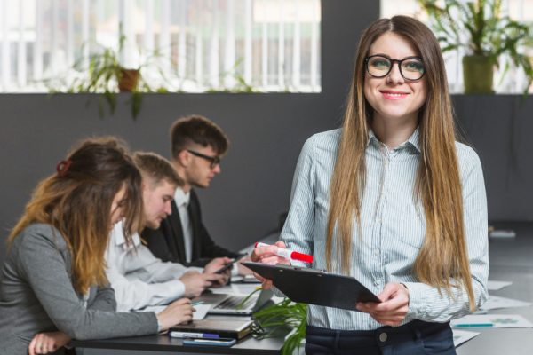 smiling-young-businesswoman-in-front-of-colleagues-working-in-office